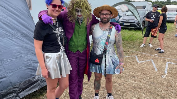 Ein als Clown verkleideter Besucher des "Reload" Festival in Sulingen posieren mit zwei Frauen im Arm für ein Foto. © NDR Foto: Andreas Gervelmeyer