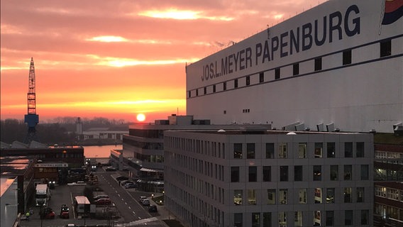 Die Sonne geht frühmorgens hinter dem Hauptgebäude der Meyer Werft in Papenburg auf. Foto: Oliver Gressieker
