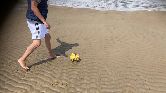 Eine Person spielt Fußball an einem Strand. © NDR Foto: Joern Pietschke