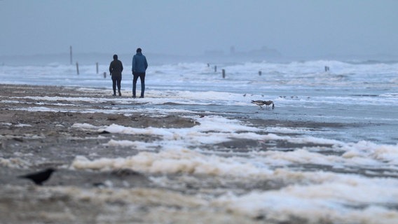 Spaziergänger laufen bei stürmischen Wetter am Nordstrand der ostfriesischen Insel Norderney. © Volker Bartels/dpa Foto: Volker Bartels