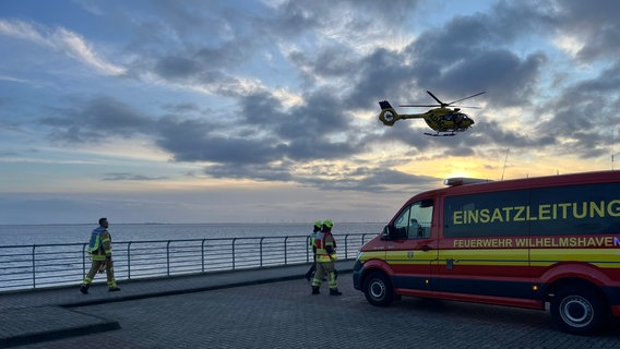 Rettungskräfte laufen zu einem Einsatzwagen, in der Luft fliegt ein Hubschrauber © Stadt Wilhelmshaven 