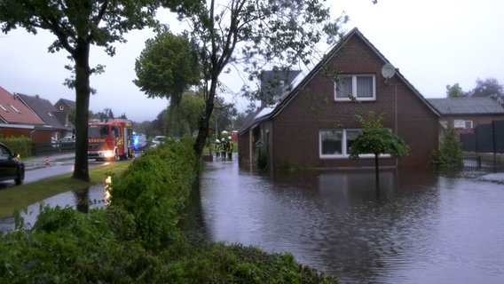 Feuerwehrleute stehen nach Starkregen neben einem Haus in Ostfriesland, im Garten steht Wasser. © NonstopNews 