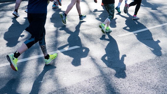 Mehrere Füße in Joggingschuhen laufen über eine asphaltierte Straße. © picture alliance / Julian Stratenschulte/dpa | Julian Stratenschulte Foto: Julian Stratenschulte