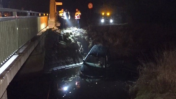 Nach einem Unfall liegt ein Auto in einem Fluss in Westerstede, Rettungskräfte beleuchten die Unfallstelle. © NonstopNews 