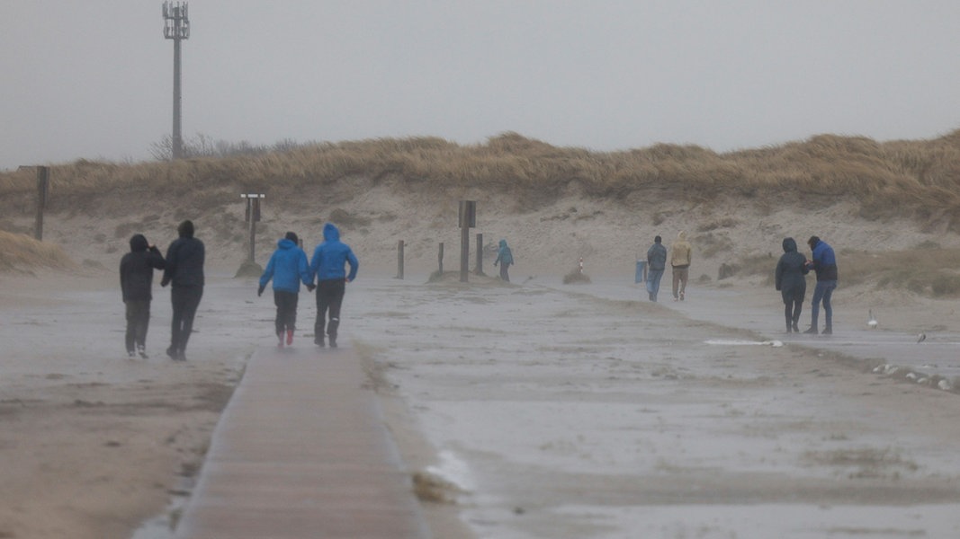 Spaziergänger gehen bei Wind am Strand von St. Peter-Ording entlang.