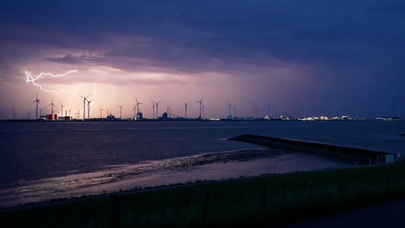 Blitze leuchten über Windkraftanlagen am Nachthimmel, aufgenommen in Emden. © Nord-West-Media TV 