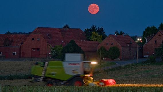 Ein rot erscheinender Mond über einem Feld, auf dem eine Landmaschine unterwegs ist. © NDR Foto: Wolfram Guder