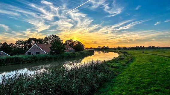 Sonnenuntergang an einem Flusslauf hinter einem Haus. © NDR Foto: Gerrit Denekas