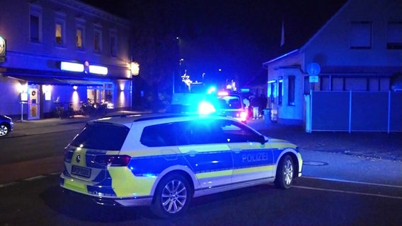 Ein Polizeiwagen steht im Dunkeln auf einer Straße, im Hintergrund weitere Einsatzwagen und Menschen. © Screenshot 