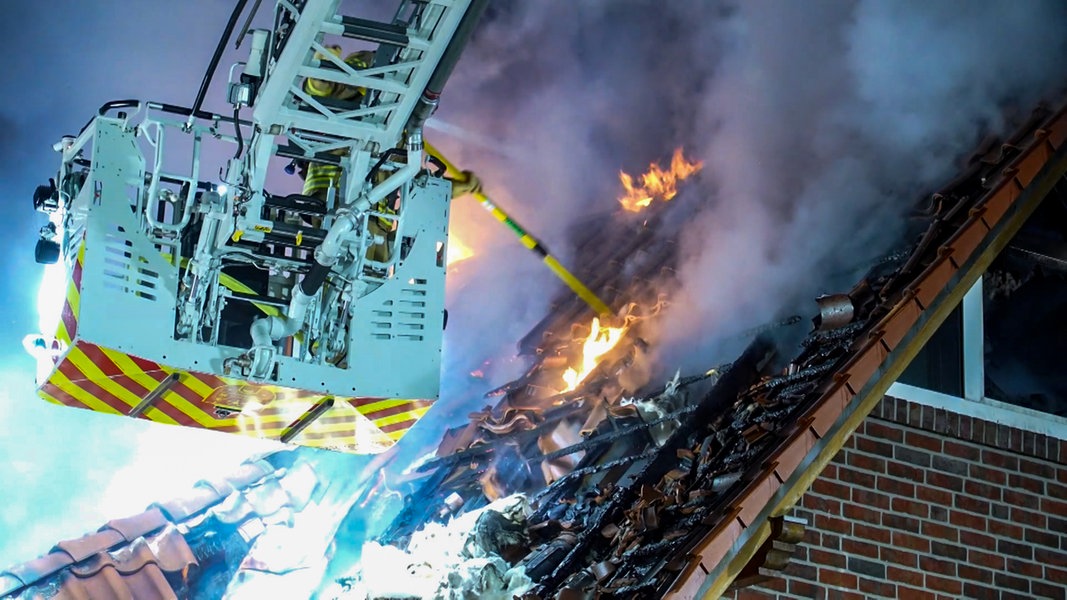 Ein Feuerwehrmann auf einer Drehleiter bekämpft den Brand in einem Haus in Wildeshausen.