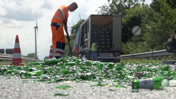 Ein Mann fegt Glasscherben von der A29, nachdem Bierkästen von der Ladefläche eines Lkw gefallen sind. © Nord-West-Media TV 