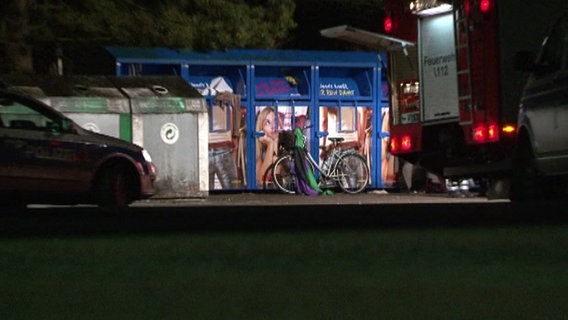 Ein Fahrrad steht vor mehreren Altkleidercontainern. Im Vordergrund stehen ein Polizeiauto sowie ein Einsatzwagen der Feuerwehr. © Nord-West-Media TV 