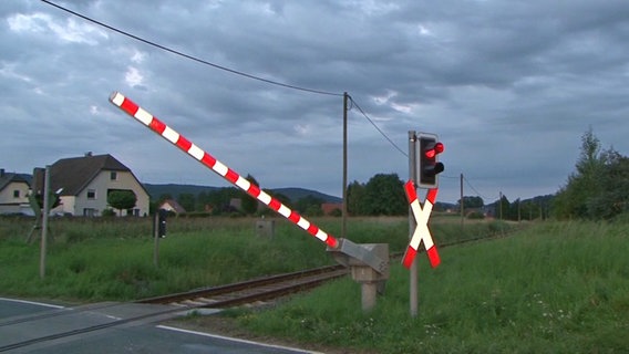 An einem Bahnübergäng mit Andreaskreuz leuchtet die Ampel rot; die Schranke ist halb geschlossen. © Nord-West-Media TV 