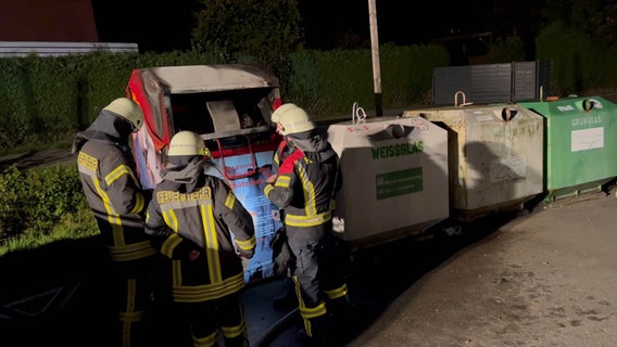 Feuerwehrleute stehen vor einem ausgebrannten Altkleidercontainer. © Nord-West-Media TV 