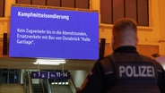 Ein Polizist steht im Osnabrücker Bahnhof vor einer Anzeigetafel, die auf eine Bombenräumung hinweist. © dpa Foto: Friso Gentsch