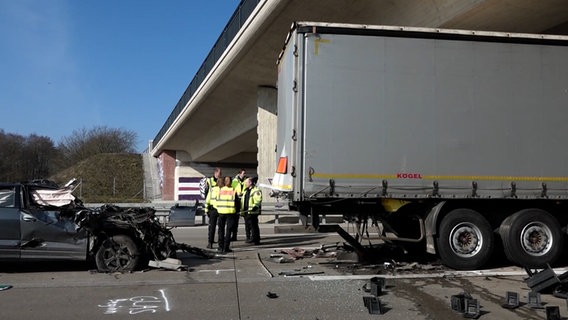 Nach einem tödlichen Unfall auf der A1 bei Holdorf steht ein stark beschädigtes Auto hinter einem Lkw, Polizeikräfte stehen daneben. © NonstopNews 