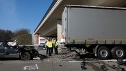 Nach einem tödlichen Unfall auf der A1 bei Holdorf steht ein stark beschädigtes Auto hinter einem Lkw, Polizeikräfte stehen daneben. © NonstopNews 