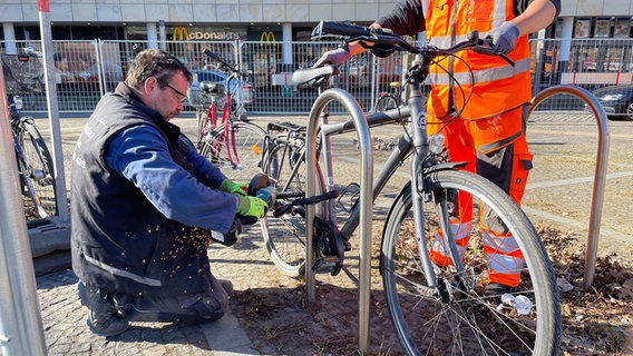 Zwei Männer flexen das Schloss eines Fahrrads am Bahnhof in Osnabrück auf. © NDR Foto: Finn Tönjes