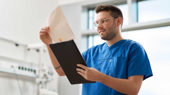 Ein Pfleger steht in einem Krankenhauszimmer und schaut auf Protokolle. © Klinikum Osnabrück 