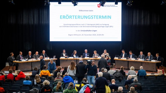 Mitarbeiter von ANF und Besucher sitzen und stehen beim Erörterungstermin in Lingen in einer Halle. © picture alliance/epd-bild Foto: Detlef Heese