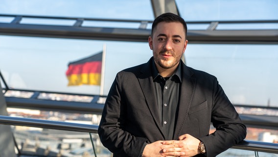 Der SPD-Politiker Manuel Gava steht im Reichstag mit einer Deutschlandfahne im Hintergrund. © Büro Manuel Gava Foto: Tobias von dem Berge