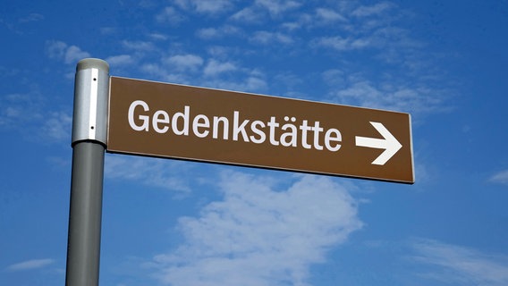 Ein braunes Schild mit der Aufschrift "Gedenkstätte" hebt sich von einem blauen Himmel ab. © picture alliance / ZB | Sascha Steinach Foto: Sascha Steinach