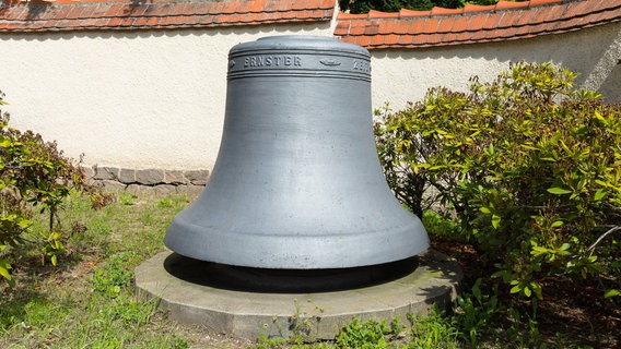 Eine Glocke steht in einem Garten, dahinter ist eine Mauer zu sehen. © Imago Foto: Hanke