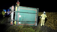 Feuerwehrleute an einem  Hühnerlaster, der auf der Seite neben einer Straße liegt. © Nord-West-Media TV 