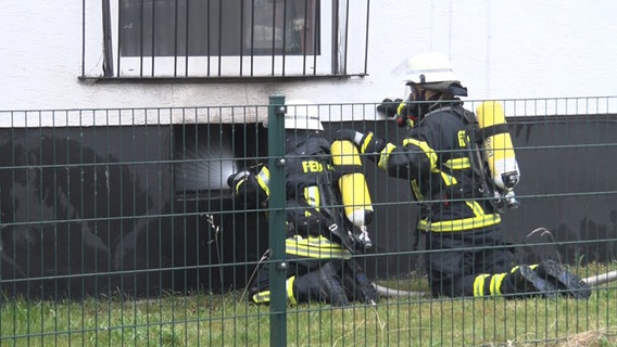 Feuerwehrleute hocken vor einem Kellerfenster in Lingen und leiten Wasser ein. © Nord-West-Media TV 