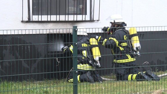 Feuerwehrleute hocken vor einem Kellerfenster in Lingen und leiten Wasser ein. © Nord-West-Media TV 