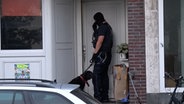 Ein maskierter Zollbeamter steht mit einem Hund vor einer Haustür. © Nord-West-Media TV 