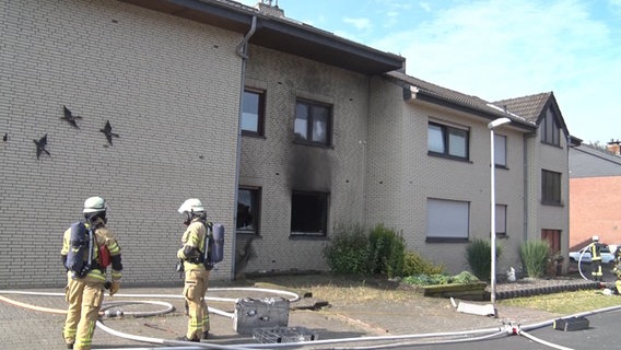 Feuerwehrleute stehen vor einem ausgebrannten Mehrfamilienhaus in Meppen. © Nord-West-Media TV 