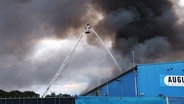 Ein Feuerwehrmann löscht auf einer Drehleiter eine brennende Lagerhalle. © NordWestMedia 