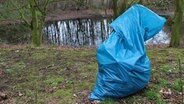 Ein blauer Müllsack steht vor einem Teich im Wald. © NDR Foto: Britta Nareyka