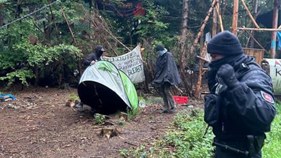 Ein Polizeibeamter steht in einem Protestcamp in einem Waldstück. © Polizei Osnabrück 