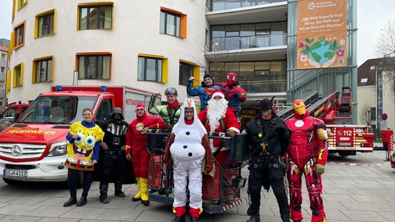 Eine Gruppe als Superhelden verkleidete Feuerwehrleute stehen vor dem Kinderkrankenhaus in Osnabrück. © NDR Foto: Andreas Gervelmeyer