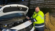 Martin Weimer ist mobiler Tankwart und leuchtet mit dem Handy in den geöffneten Motorraum eines weißen Transporters. © NDR Foto: Andreas Gervelmeyer