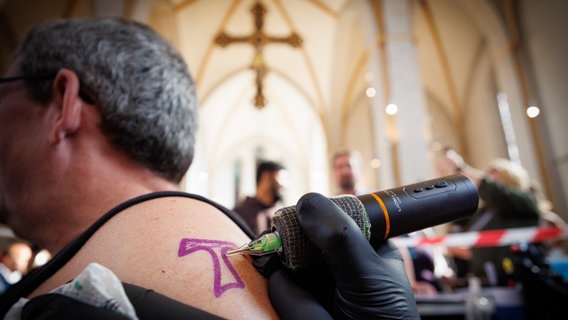 Osnabrück: Der Arm eines Mannes wird bei einem Tattoo-Gottesdienst in der Johanniskirche mit einem Kreuz tätowiert. © dpa-Bildfunk Foto: Friso Gentsch