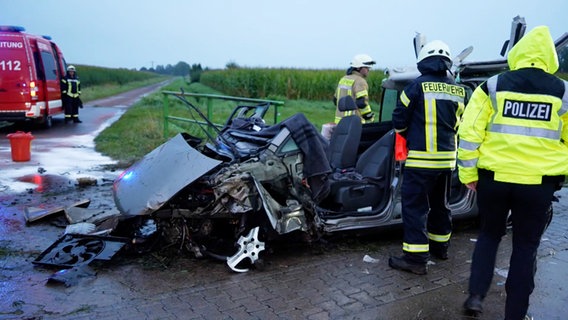 Ein Polizist und zwei Feuerwehrleute stehen vor einem Autowrack nach einem in Wagenfeld. © Nord-West-Media TV 