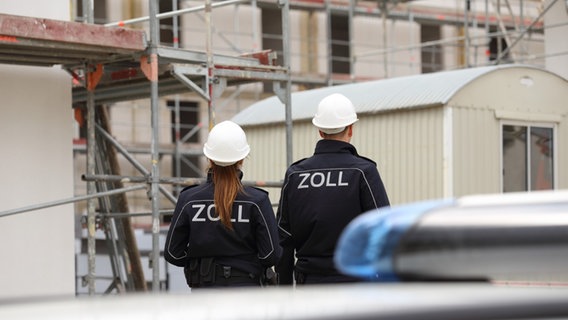 Eine Zollbeamtin und ein Zollbeamter von hinten gesehen laufen über eine Baustelle. © Hauptzollamt Osnabrück 