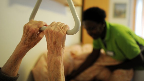 Eine Pflegekraft hilft einer Pflegehausbewohnerin beim Hinlegen. © dpa-Bildfunk Foto: Angelika Warmuth