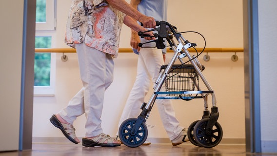 Eine Pflegekraft geht in einem Pflegeheim mit einer älteren Dame über einen Korridor. © picture alliance/dpa Foto: Christoph Schmidt