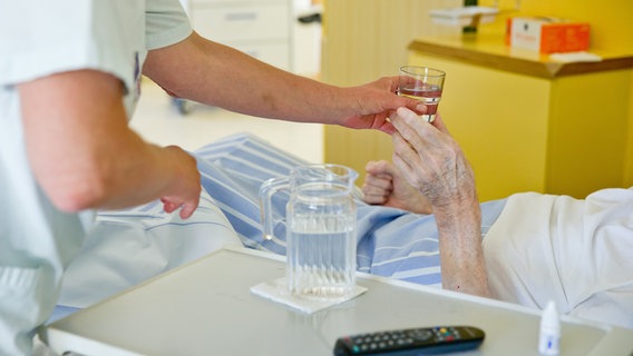 Eine Krankenpflegerin reicht einem Patienten in einem Krankenhaus ein Glas Wasser. © picture alliance/dpa | Daniel Karmann Foto: Daniel Karmann