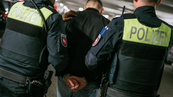 Zwei Einsatzkräfte der Polizei führen einen Mann mit angelegten Handschellen ab. © NDR Foto: Julius Matuschik