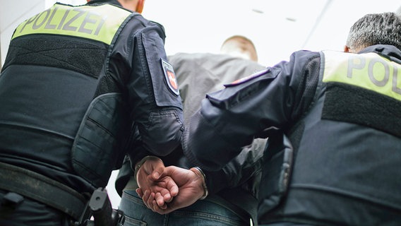 Zwei Einsatzkräfte der Polizei führen einen Mann mit angelegten Handschellen ab. © NDR Foto: Julius Matuschik