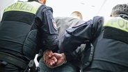 Zwei Einsatzkräfte der Polizei führen einen Mann mit angelegten Handschellen ab. © NDR Foto: Julius Matuschik