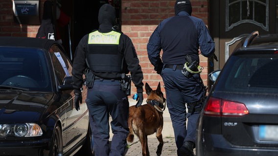 Polizisten gehen mit einem Spürhund auf ein Haus in Melle zu. © dpa Foto: Friso Gentsch