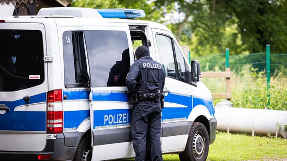 Ein Polizist steht am 13. Juni 2024 während einer Razzia auf einem Hof bei Espelkamp an einem Einsatzfahrzeug. © dpa-Bildfunk Foto: Moritz Frankenberg