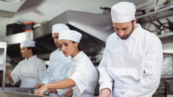 Köchinnen und Köche stehen in der Küche eines Restaurants und bereiten Essen zu. © picture alliance/Zoonar Foto: Channel Partners