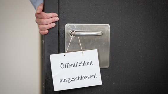 Ein Justizbeamter schließt die Tür eines Gerichtssaals, an der ein Schild mit dem Aufdruck Öffentlichkeit ausgeschlossen hängt. © picture alliance / dpa Foto: Friso Gentsch